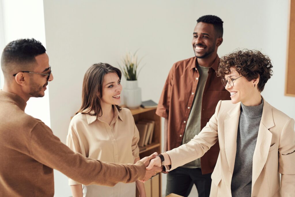 Four colleagues smiling and shaking hands in a bright office setting.