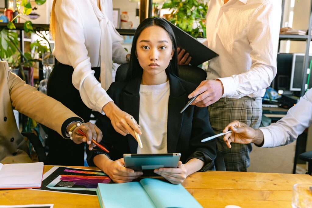 An overwhelmed office worker surrounded by colleagues requesting her attention during a busy workday.